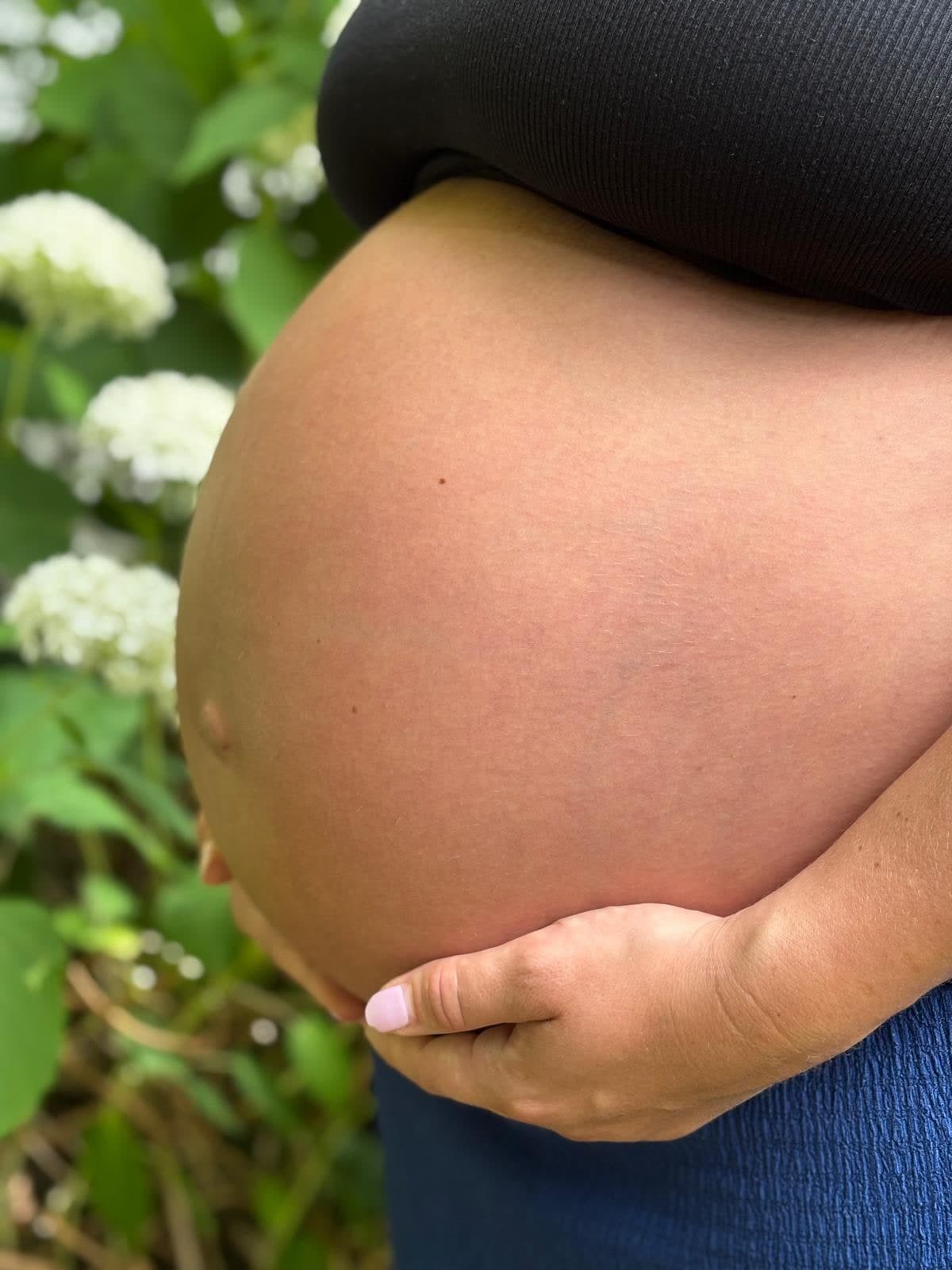 Ventre de femme enceinte devant des hortensias blancs