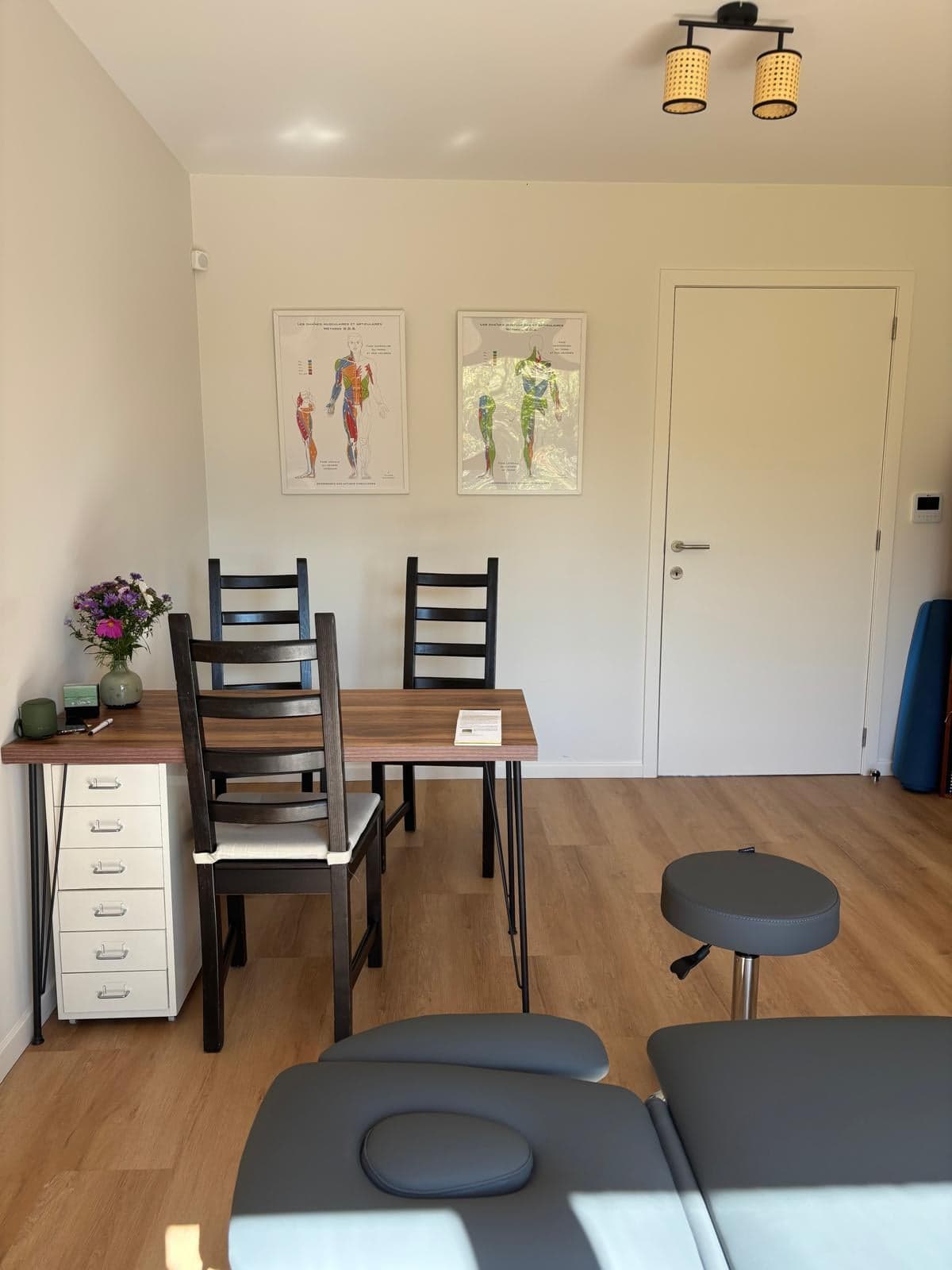 Coin bureau du cabinet avec table en bois, chaises et planches des chaînes musculaires GDS au mur